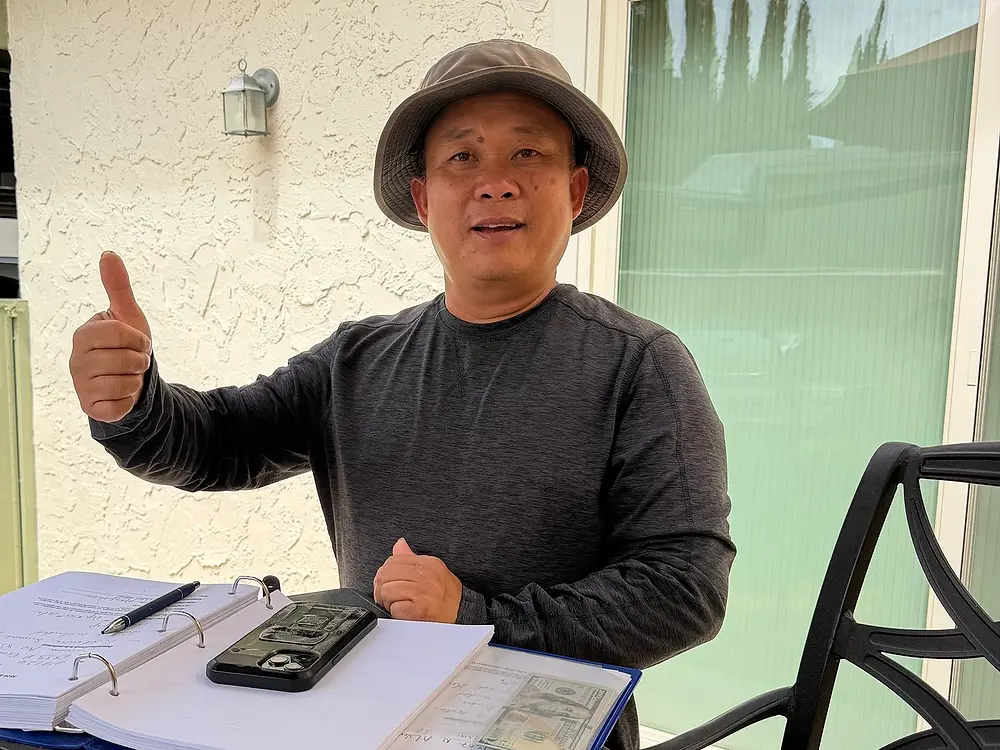 Chris Nguyen, owner of Q&T Services, giving a thumbs up at a table with his estimate binder